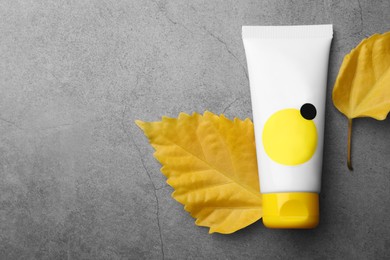 Photo of Tube of face cream and yellow leaves on grey table, top view. Space for text