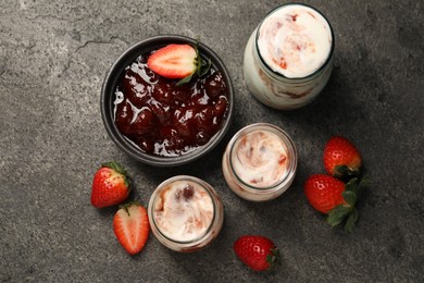 Photo of Tasty yoghurt with jam and strawberries on grey textured table, top view