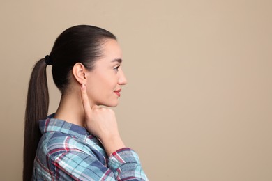 Photo of Young woman pointing at her ear on beige background. Space for text