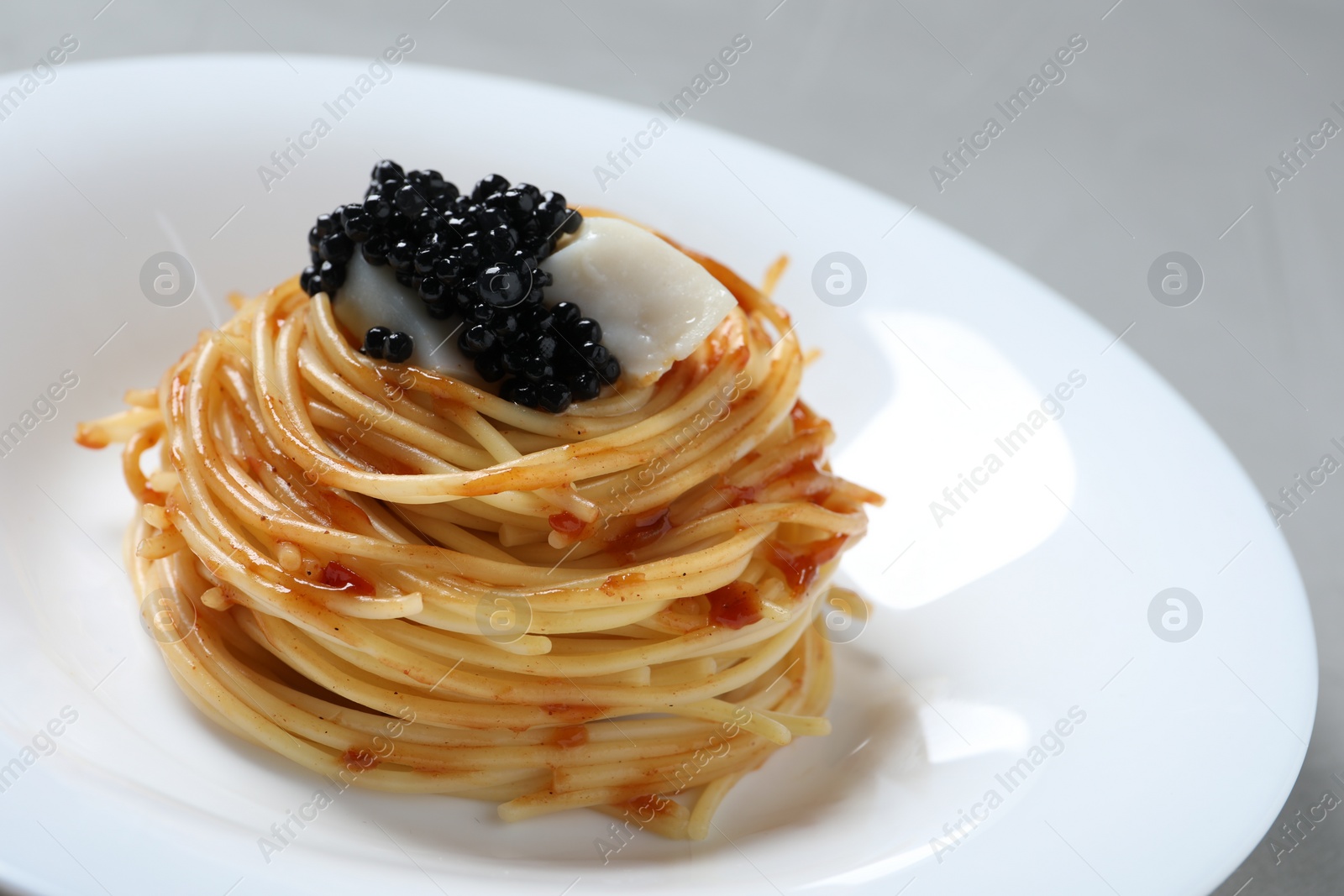 Photo of Tasty spaghetti with tomato sauce and black caviar on plate, closeup. Exquisite presentation of pasta dish