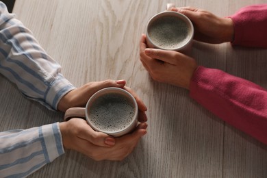 Photo of Women with cups of hot coffee at light wooden table, closeup