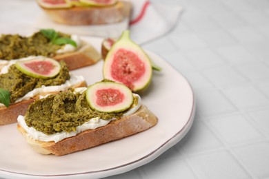 Photo of Tasty bruschettas with cream cheese, pesto sauce, figs and fresh basil on white table, closeup. Space for text