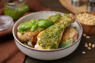 Delicious fried chicken drumsticks with pesto sauce and basil in bowl on table, closeup