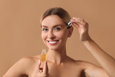 Beautiful woman applying cosmetic serum onto her face on beige background