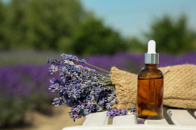 Photo of Bottle of essential oil and lavender flowers on white wooden surface outdoors, space for text