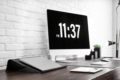 Modern workplace interior with computer and devices on table near brick wall