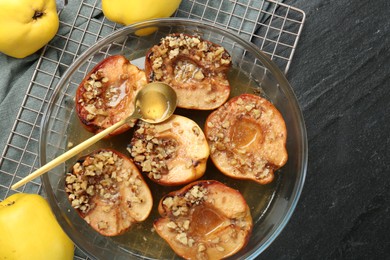 Photo of Tasty baked quinces with walnuts and honey in bowl on black table, flat lay