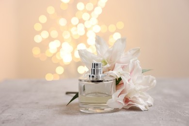 Bottle of perfume and beautiful lily flowers on table against beige background with blurred lights