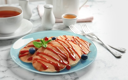 Tasty pancakes with berries and syrup on table