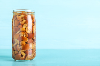 Glass jar of pickled mushrooms on light blue wooden table. Space for text