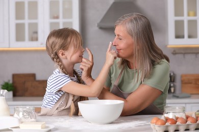 Happy grandmother with her granddaughter having fun while cooking together in kitchen