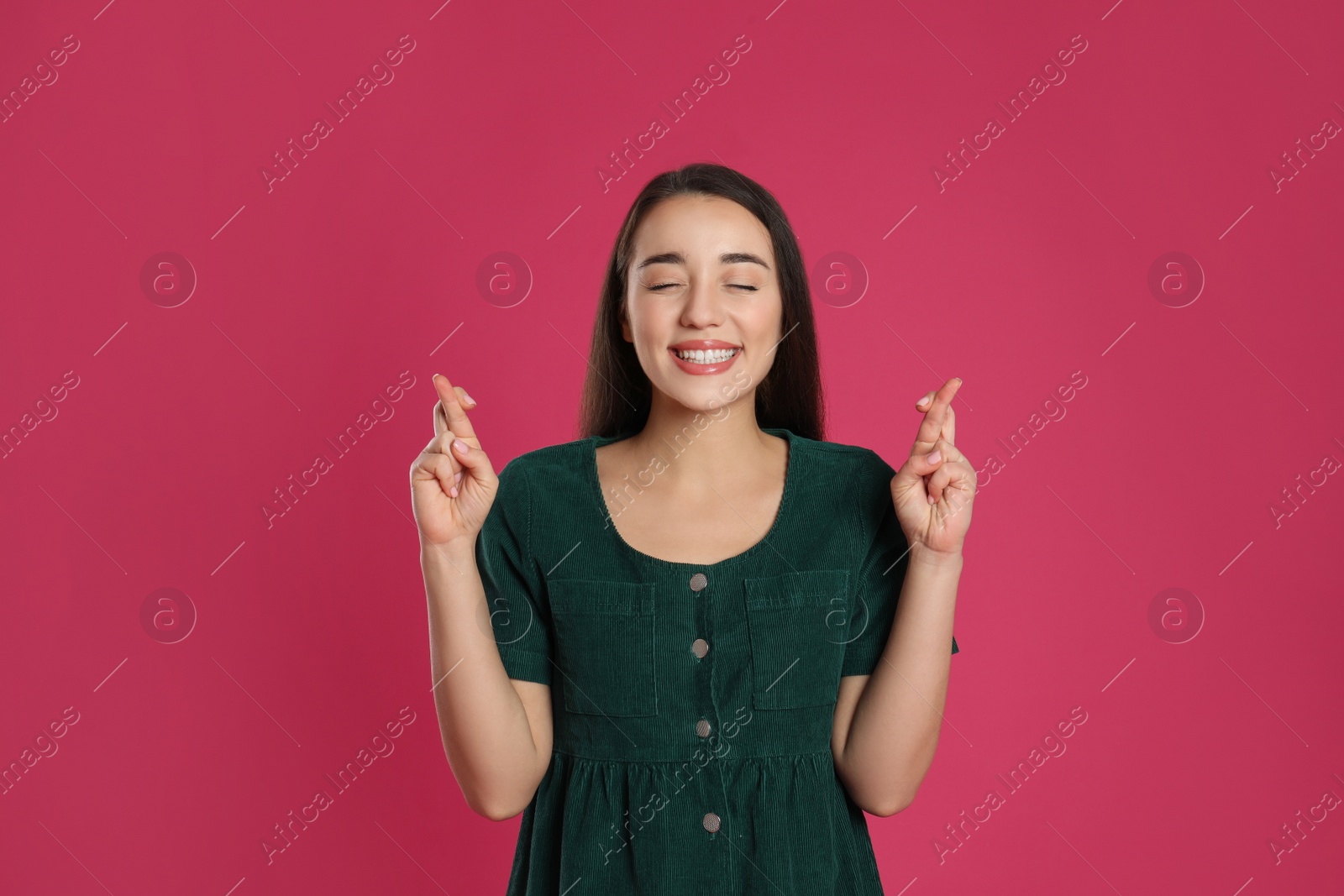 Photo of Woman with crossed fingers on pink background. Superstition concept