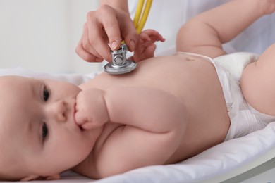 Pediatrician examining cute little baby with stethoscope in clinic, closeup