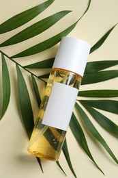 Photo of Bottle with cosmetic oil and green leaf on beige background, top view