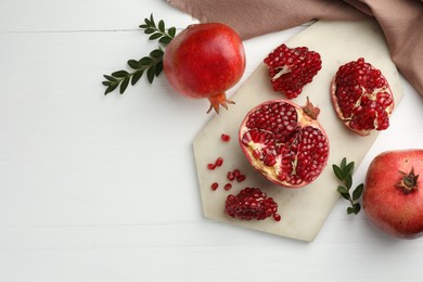 Photo of Fresh pomegranates and branches on white wooden table, flat lay. Space for text