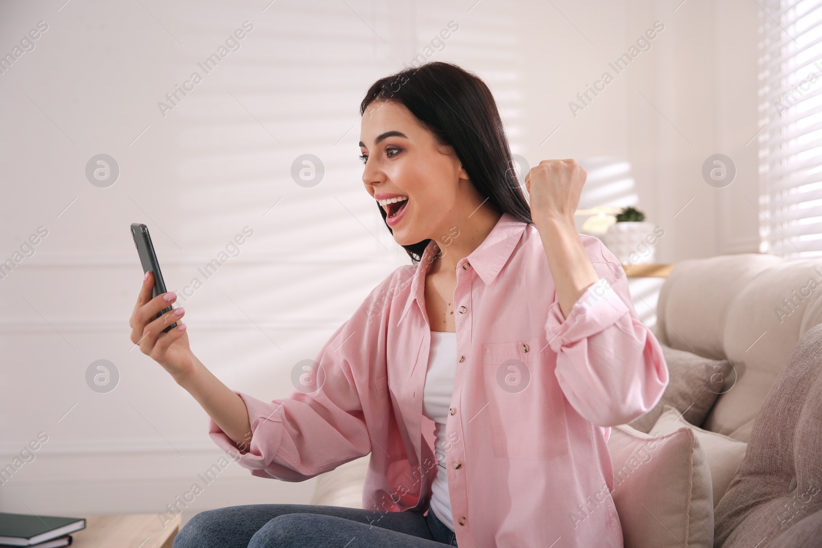 Photo of Emotional woman participating in online auction using smartphone at home