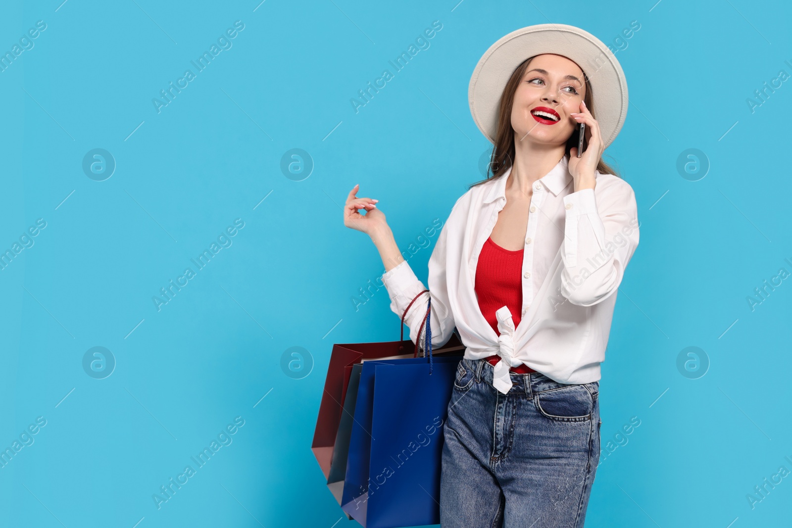 Photo of Stylish young woman with shopping bags talking on smartphone against light blue background, space for text