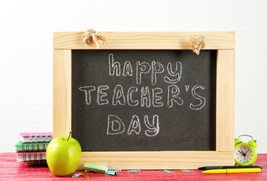 Little blackboard with inscription HAPPY TEACHER'S DAY, apple and stationery on table