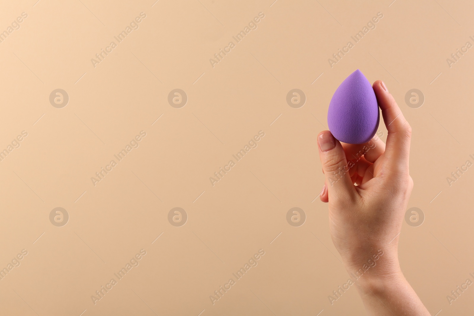 Photo of Woman with purple makeup sponge on beige background, closeup. Space for text