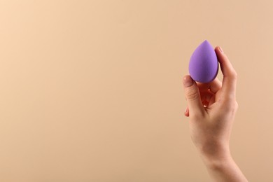 Photo of Woman with purple makeup sponge on beige background, closeup. Space for text