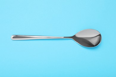 Photo of One shiny silver spoon on light blue background, top view