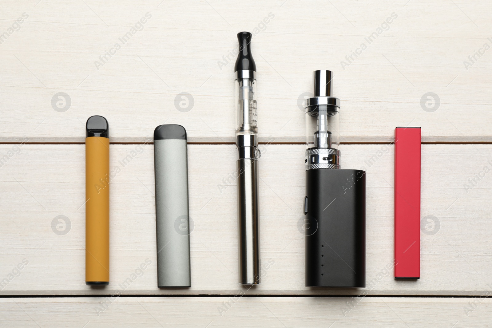 Photo of Different electronic cigarettes on white wooden table, flat lay. Smoking alternative