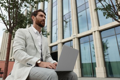 Handsome businessman with laptop on city street