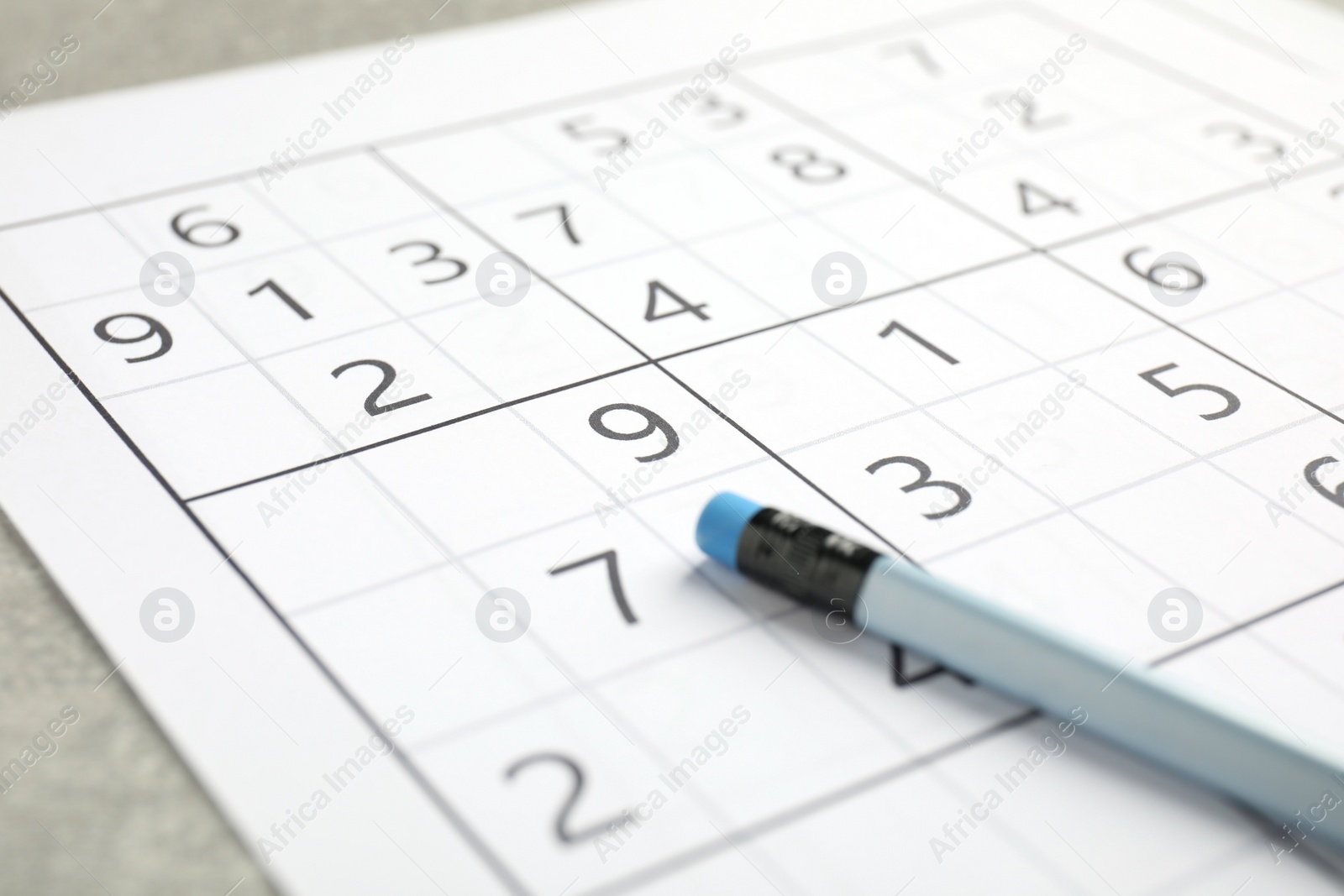 Photo of Sudoku and pencil on grey table, closeup