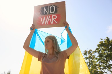 Photo of Sad woman holding poster with words No War and Ukrainian flag outdoors
