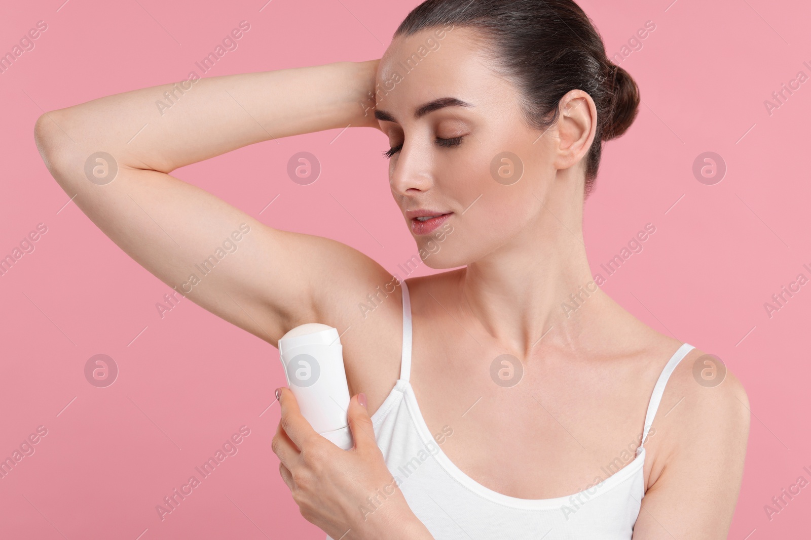 Photo of Beautiful woman applying deodorant on pink background