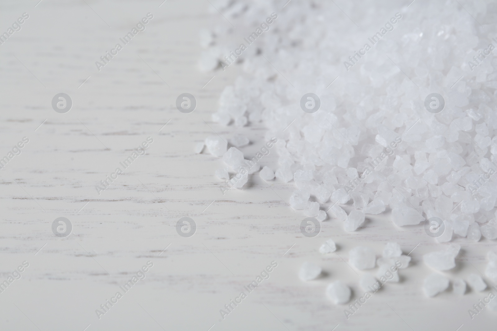 Photo of Natural sea salt on white wooden table, closeup. Space for text