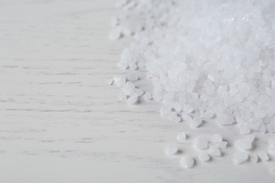 Photo of Natural sea salt on white wooden table, closeup. Space for text