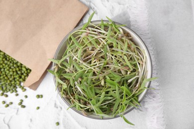 Photo of Bowl with sprouts and mung beans on white textured table, flat lay