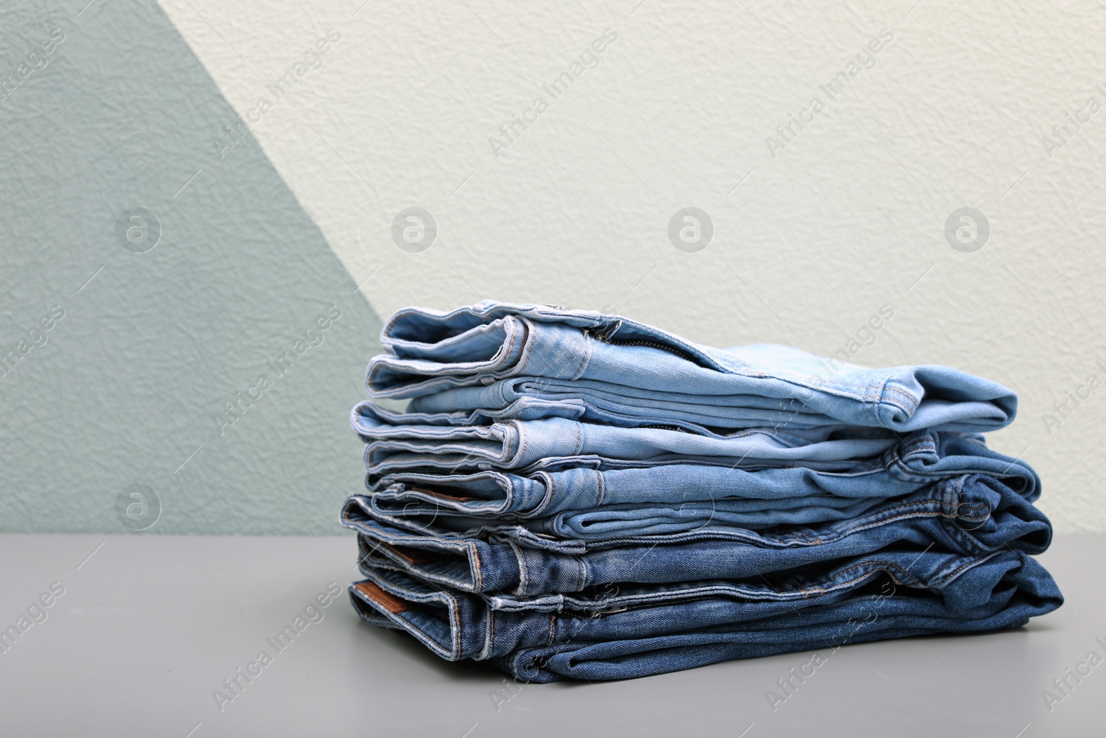 Photo of Stack of stylish jeans on table against color wall