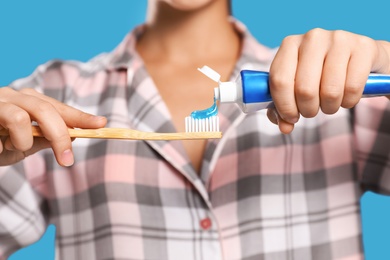 Woman applying toothpaste on brush against blue background, closeup