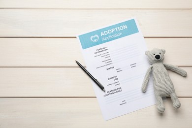 Photo of Adoption application, toy bear and pen on white wooden table, flat lay. Space for text