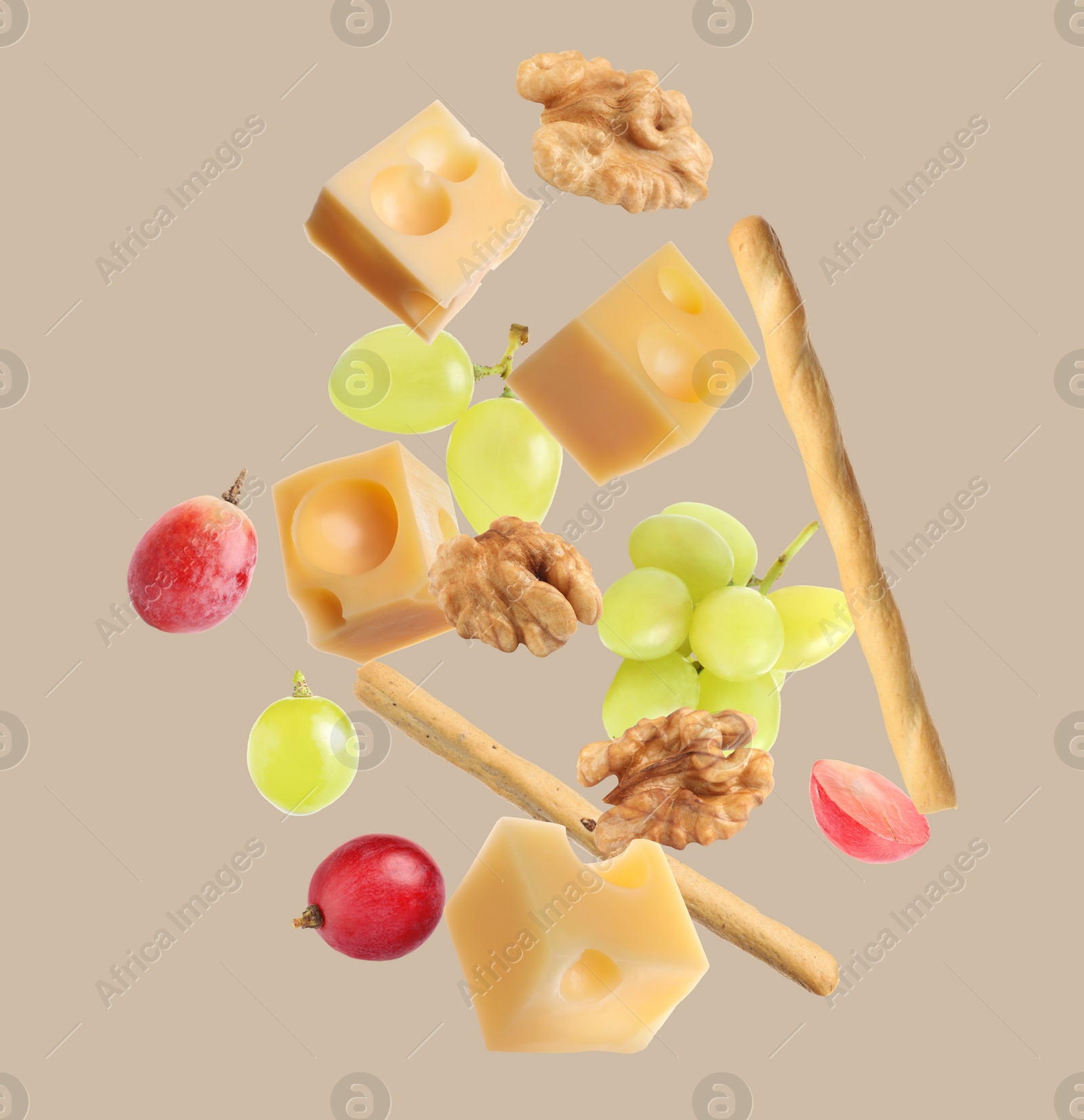 Image of Cheese, breadsticks, grapes and walnuts falling against beige background