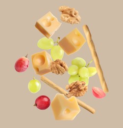 Image of Cheese, breadsticks, grapes and walnuts falling against beige background