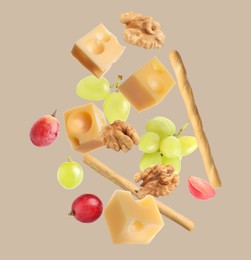 Cheese, breadsticks, grapes and walnuts falling against beige background