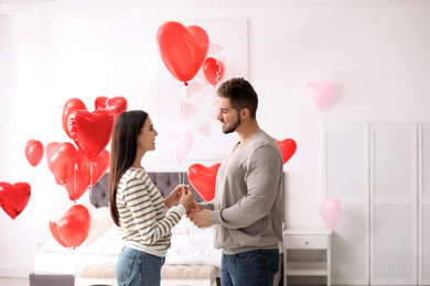 Photo of Lovely young couple in bedroom decorated with heart shaped balloons. Valentine's day celebration