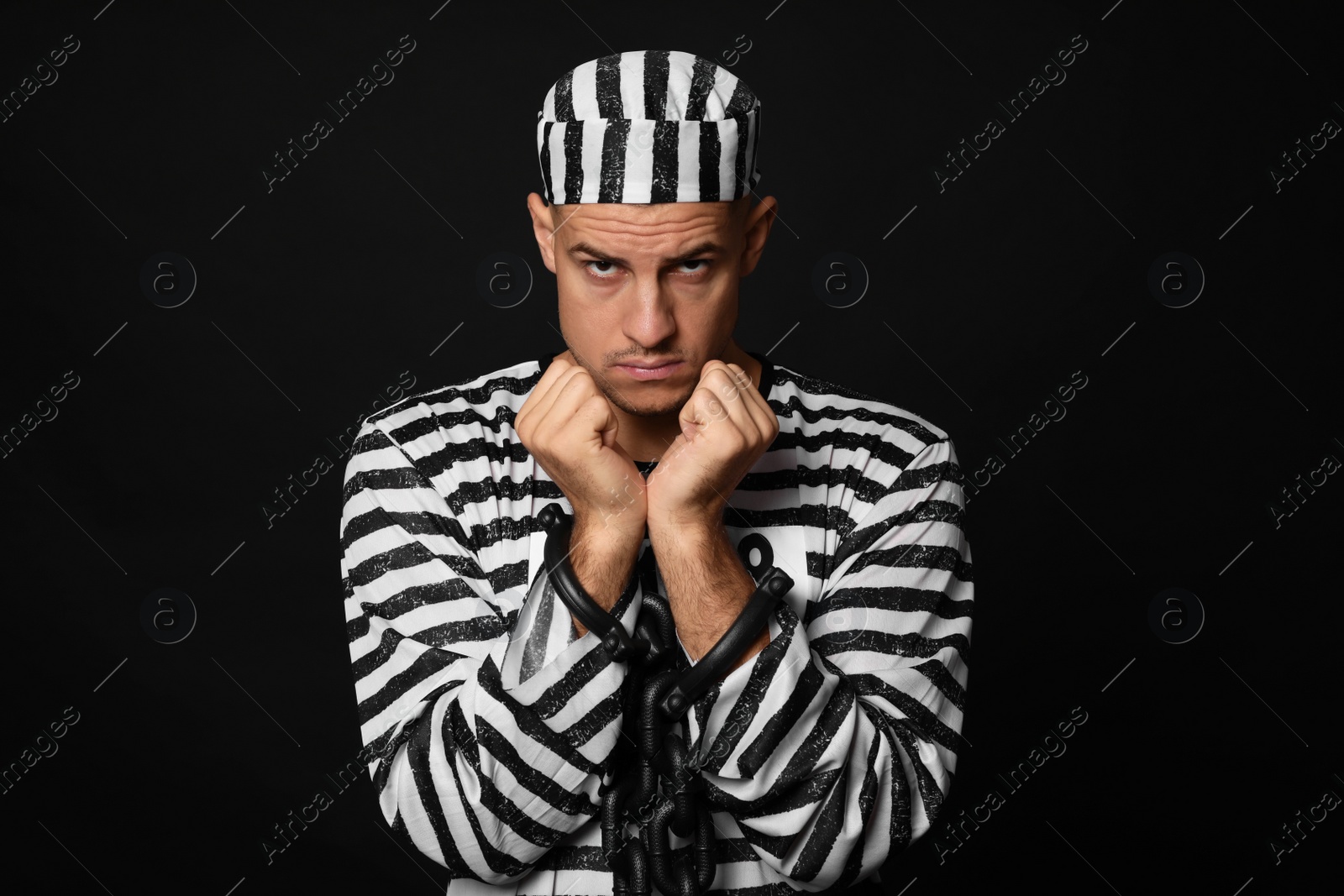 Photo of Prisoner in striped uniform with chained hands on black background