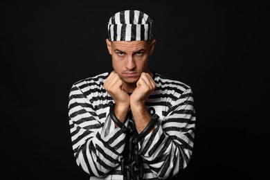 Photo of Prisoner in striped uniform with chained hands on black background