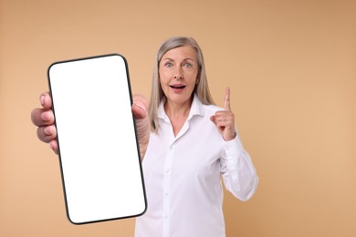 Image of Mature woman showing mobile phone with blank screen on beige background. Mockup for design