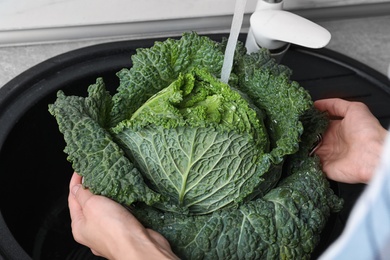 Photo of Woman washing fresh green savoy cabbage under tap water in kitchen sink, closeup