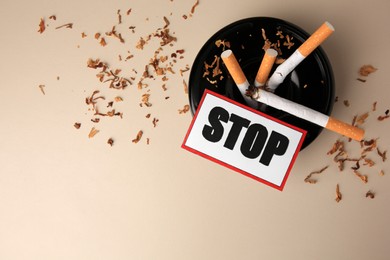 Card with word Stop, ashtray and cigarette stubs on beige background, flat lay with space for text. Quitting smoking concept