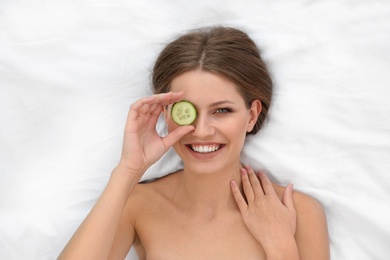 Photo of Beautiful woman with cucumber slice on white fabric, above view. Organic face mask