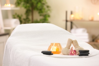 Photo of Composition with herbal bags, candle and stones on massage table in spa salon