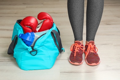 Photo of Young woman in sportswear and bag with gym equipment indoors