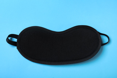 Photo of Black sleeping mask on light blue background, top view. Bedtime accessory