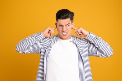 Emotional man covering ears with fingers on yellow background